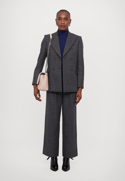 Blazer grigio doppiopetto, pantaloni larghi coordinati, dolcevita blu navy e borsa trapuntata rosa chiaro con tracolla a catena. Stivali neri con tacco.