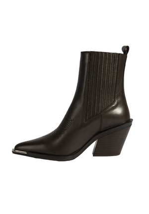 Bottine en cuir marron avec bout pointu, rainures verticales sur les côtés et talon empilé. Équipée d'un accent métallique à l'avant.