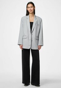 Gai pelēks pārmērīgs žakets ar divām pogām, izgrieztiem atlociem un priekšējiem kabatām, apvienots ar melniem platām biksēm. Gluda tekstūra.