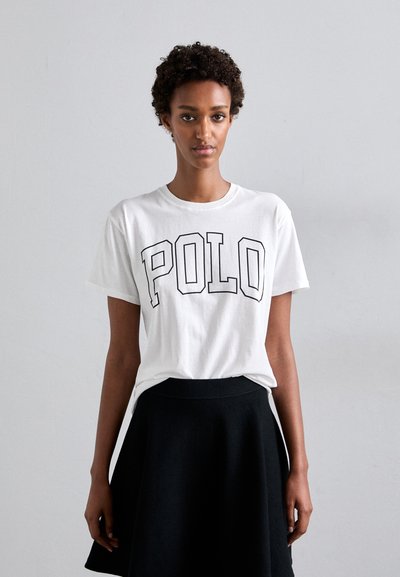 Hvid bomulds T-shirt med fed sort "POLO" brodering, korte ærmer, rund halsudskæring. Kombineret med en sort knælang nederdel.