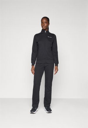 Zwarte fleecejack met rits en bijpassende broek. Soepele textuur, aansluitend ontwerp, minimale branding op de borst en sneakers met rubberen zolen.
