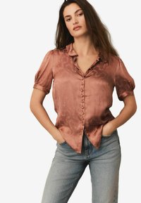 Satin, rustfarvet bluse med blomstermønster, korte opsmøgede ærmer og knaplukning foran. Sammen med lyseblå jeans.