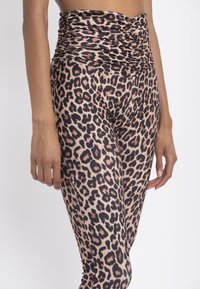 Leggings con stampa leopardata caratterizzati da un alto cinturino arricciato, realizzati in tessuto elastico con una superficie liscia, principalmente nei colori beige, nero e marrone.