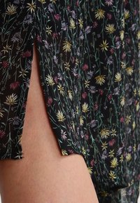 Czarna sukienka w kwiaty z przezroczystej, lekkiej tkaniny; charakteryzuje się kolorowymi wzorami kwiatów oraz bocznymi rozcięciami dla dodatkowego stylu.