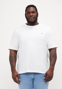 Hvit kortermet t-skjorte laget av bomull, med rund hals og en liten logo på brystet. Kombinert med lyseblå jeans.
