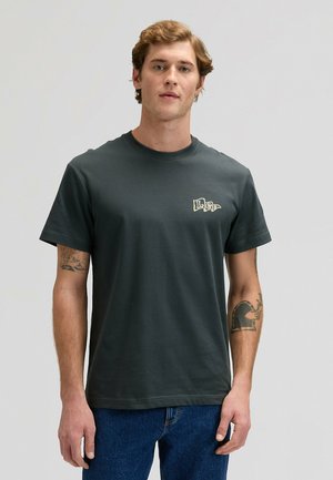 Ciemnoszara bawełniana koszulka z okrągłym dekoltem, krótkimi rękawami i małym haftowanym logo na lewej piersi. Nosi się ją z niebieskimi dżinsami.