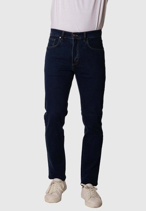 Jeans de mezclilla azul marino con corte ajustado, diseño de cinco bolsillos y detalles de costura visibles. Combinados con zapatillas blancas.