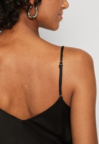 Camisole en satin noir avec des bretelles fines ajustables, présentant un décolleté dos en V. Texture lisse et design minimaliste.