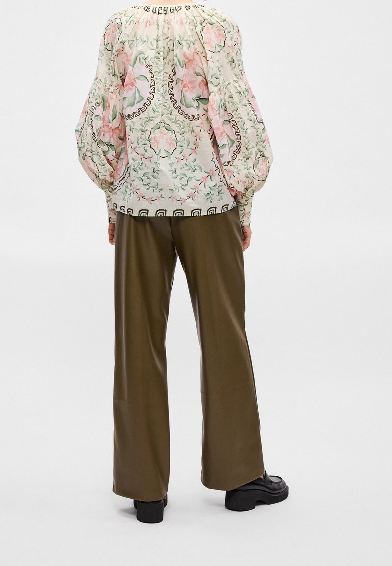 Femme portant un chemisier à manches longues fleuri avec des manches ballon et un pantalon large vert olive, vue de dos.