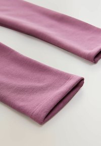 Vaaleanpunaiset puuvillaiset legginsit, joissa on sileä rakenne ja käännetyt hihansuut. Suunnittelu on yksinkertainen ilman kuvioita tai koristeita.