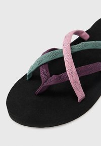 Sorte flate såler sandaler med tre vevde stropper i grønn, lilla og rosa. Stropperne har teksturerte mønstre for bedre grep.