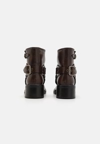 Botine din piele maro, cu finisaj mat, dotate cu catarame laterale, accente cu tinte și toc gros negru. Talpa texturată pentru aderență.