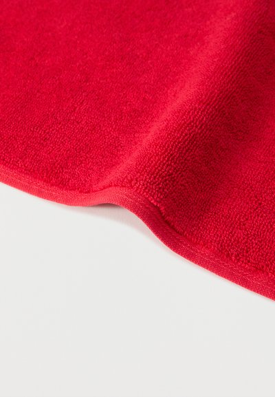 Φωτεινή κόκκινη πετσέτα από πετσέτα με υφή βρόχων, διπλωμένη πάνω σε λευκή επιφάνεια που δείχνει λεπτομέρειες ραμμένης άκρης.