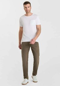 T-shirt en coton blanc avec une poche avant texturée, associée à un pantalon vert olive et des baskets blanches avec une semelle beige.