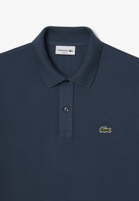 Polo marino en tejido texturizado, con botonera de dos botones y un pequeño logo bordado de cocodrilo verde en el lado izquierdo del pecho.