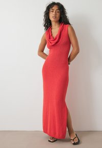 Punane kootud maksikleit, millel on kaelus ja külgmine lõhik. Omab tekstuuriga kangast ja ilma varrukateta disaini, mis on ühendatud mustade sandaalidega.