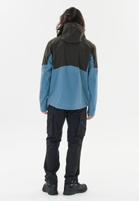 Vattentålig blå jacka med en svart överdel, mjuk textur, justerbar huva, kombinerad med svarta cargobyxor och robusta stövlar.
