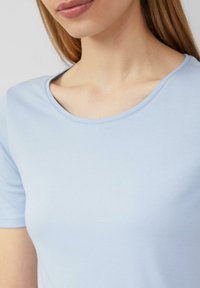 T-shirt bleu clair à manches courtes avec un col rond et une texture lisse. Le tissu paraît doux et ajusté autour des épaules.