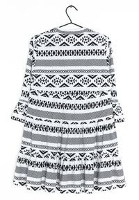 Černobílé šaty s dlouhými rukávy, zdobené geometrickými vzory a volánkovým lemem, vyrobené z lehkého materiálu.