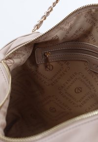 Beige quiltet håndtaske indvendig med en guldfarvet lynlås, featuring en lille lynlås lomme og trykt logo mønster på foret.