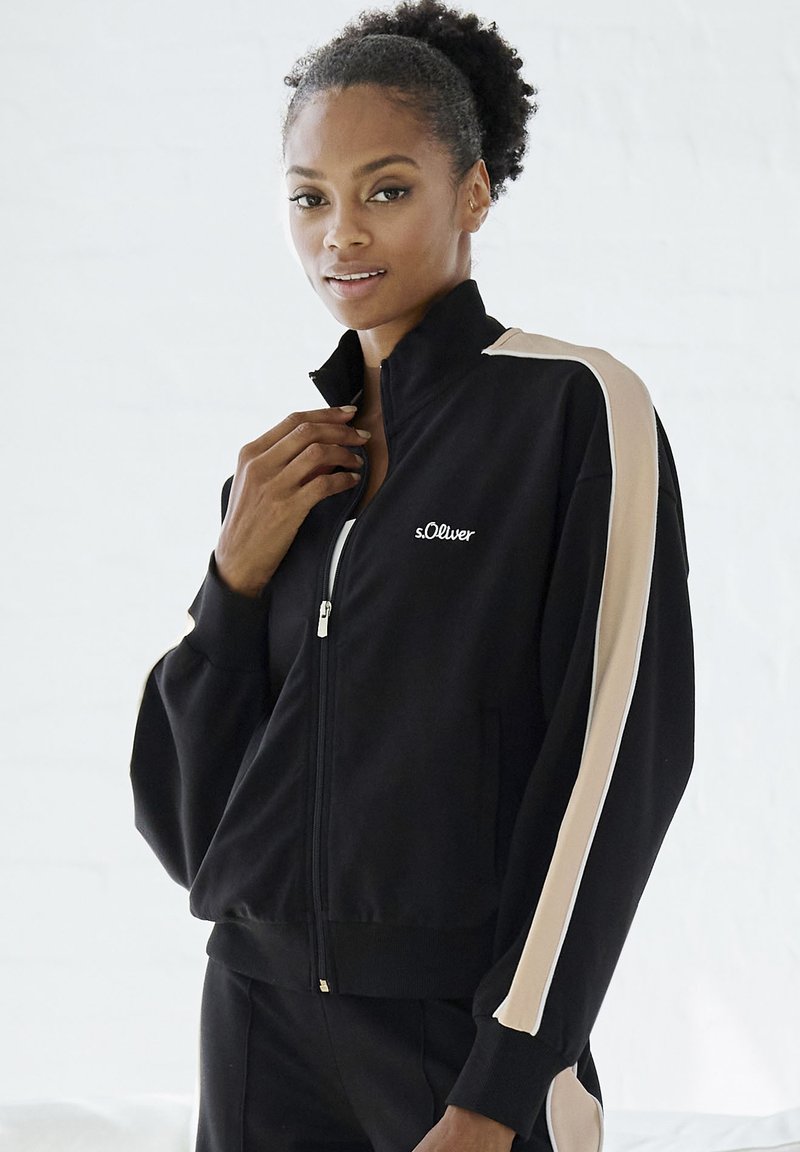 Schwarze Zip-Jacke mit beigen Seitenstreifen, aus einem weichen Material gefertigt. Verfügt über einen Stehkragen und das Markenlogo auf der Vorderseite.