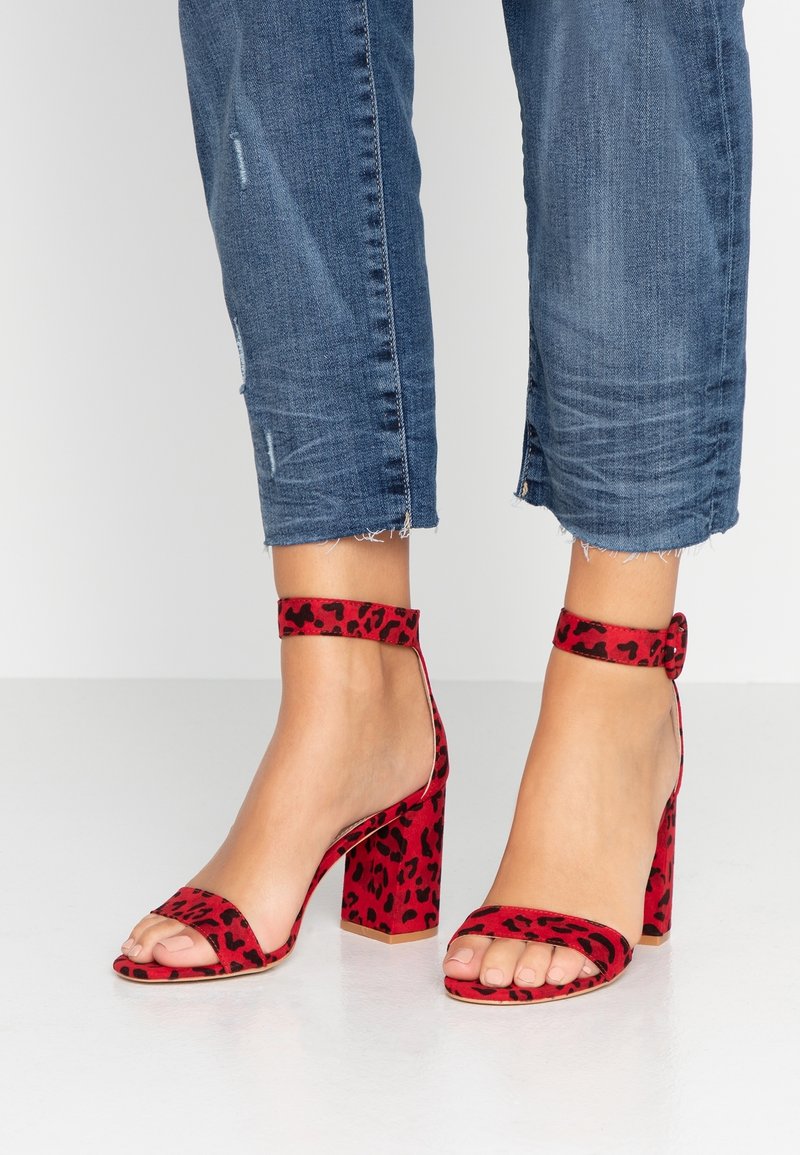 Sandales à talons rouges avec imprimé léopard, présentant une large lanière sur les orteils et une lanière de cheville, en tissu texturé, et talons blocs.