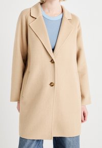 Abrigo de mezcla de lana color beige con cuello de muesca, cierre de dos botones y bolsillos laterales. Cuenta con mangas largas y un corte relajado.