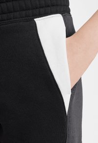 Black sweatpants feature a side pocket with a contrasting white panel. The material is soft and textured, with a ribbed waistband.