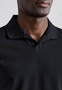 Czarna koszulka polo o miękkiej, gładkiej strukturze; ma klasyczny kołnierzyk i krótkie rękawy, zaprojektowana do noszenia na co dzień.