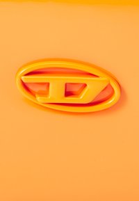 Oranžinis automobilio skyrius su blizgiu paviršiumi ir ryškiu ovaliu logotipu, kuris yra šiek tiek tamsesnės oranžinės spalvos, išryškinantis jo aerodinamišką dizainą.