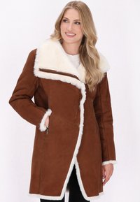Brun faux suede jakke med en hvid faux fur krave og kant. Har lynlås-lommer og et asymmetrisk frontdesign.