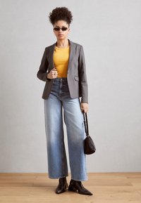 Šedý blazer přes žlutý žebrovaný top, v kombinaci s širokými světle modrými džíny a černými kotníkovými botami. Doplněno malou černou taškou a slunečními brýlemi.