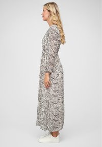 Robe maxi en tissu transparent avec des rayures zèbre noir et blanc, dotée de manches longues et d'une taille accentuée, associée à des baskets blanches.