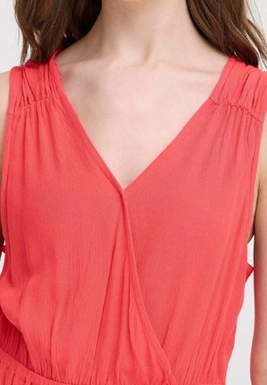 Różowa, koralowa bluzka bez rękawów z dekoltem w kształcie litery V, marszczeniami na ramionach oraz miękką, pomarszczoną tkaniną.