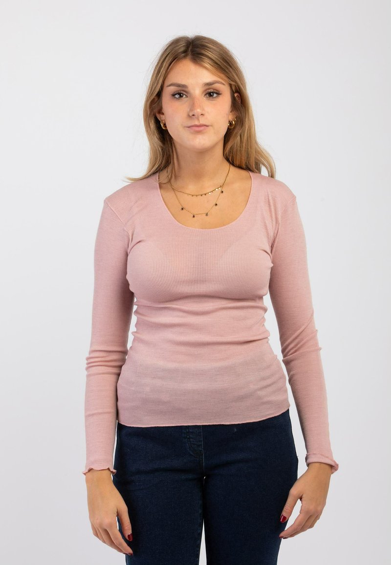 Top a maniche lunghe, aderente, in morbido tessuto a coste rosa pallido, con scollatura a barca e delicati dettagli a volant sui polsini. Abbinato a jeans scuri.