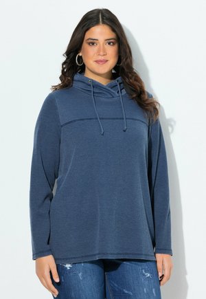 Haut à capuche bleu marine texturé avec un cordon de serrage et des manches longues. Présente une couture horizontale sur la poitrine. Associé à un jean déchiré.