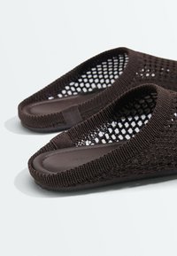 Chaussures slip-on marron foncé avec un design en maille ajourée et des semelles intérieures rembourrées solides sur une surface blanche.