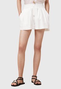 Shorts bianchi in lino con vita regolabile, tasche laterali e vestibilità rilassata. Abbinati a sandali neri con strappi.