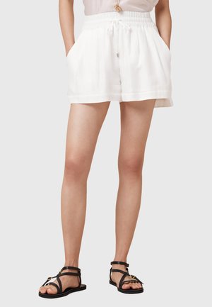 Shorts bianchi in lino con vita regolabile, tasche laterali e vestibilità rilassata. Abbinati a sandali neri con strappi.