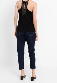 Svart ärmlös topp med en spetsdetalj på ryggen och en knapp, parat med mörkblå högmidjade jeans och svarta klackskor.