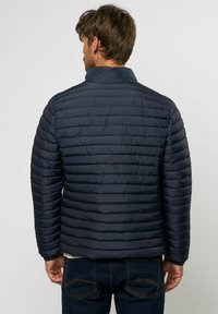 Mørkeblå puffjakke med horisontalt kviltet design, høy krage og lange ermer, laget av glatt, lett materiale.