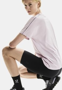 Helles rosa Sport-T-Shirt mit schwarzen Akzenten, kombiniert mit schwarzen Kompressionsshorts und schwarzen Laufschuhen mit einem auffälligen Logo.