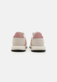 Footwear featuring a beige suede upper, contrasting pink glitter heel accents, and gold circular hardware on the sides. Rubber outsole.