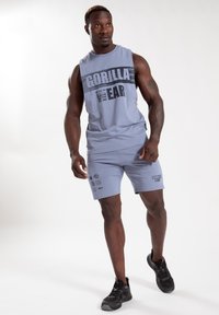 Lichtblauw tanktop met de tekst "GORILLA WEAR", gecombineerd met bijpassende shorts met grafische prints. G gedragen met zwarte sportschoenen.