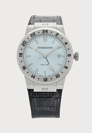 Montre bracelet Ferragamo F-80 GMT argentée avec bracelet en cuir noir, cadran bleu clair, lunette 24 heures et affichage de la date à trois heures.
