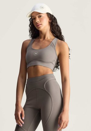 Lichtgrijze sportbeha en legging set met een gladde textuur, voorzien van gestikte accenten en een logo op de beha, aangevuld met een witte pet.