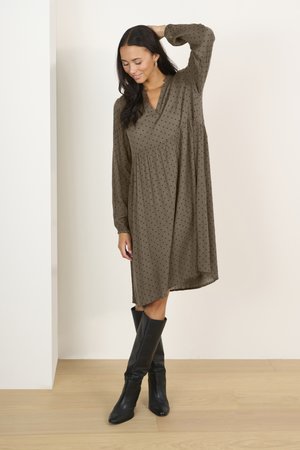 Olive green dress with polka dot pattern, long sleeves, V-neckline, and flared shape, paired with knee-high black boots.