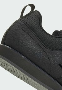 Czarny but sportowy z fakturowanym wykończeniem, siateczkową górą i gumową podeszwą. Posiada pętelkę z tyłu oraz wyraźne akcenty logo.