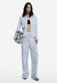 Ensemble deux pièces en tissu léger imprimé bleu clair avec motifs floraux. Comprend une chemise boutonnée, un pantalon à jambes larges et un sac à main graphique.