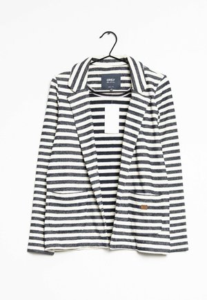 Sort-hvidt blazer med vandrette striber, revers og forlommer, hængende på en sort bøjle mod en hvid baggrund.